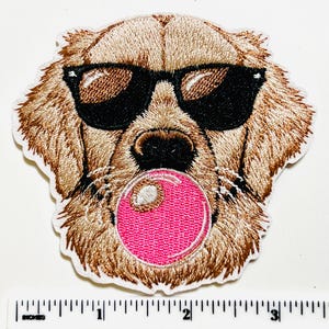 May include: Embroidered patch featuring a golden retriever dog wearing black sunglasses and blowing a pink bubble. The patch has a white border and is approximately 3 inches wide.
