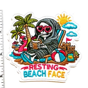 May include: Embroidered patch featuring a skeleton in a beach chair, wearing heart-shaped sunglasses and a hooded robe, enjoying a drink. The patch includes a palm tree, flamingo float, sandcastle, beach ball, and the text "RESTING BEACH FACE".