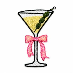 May include: An embroidered patch shaped like a martini glass with a yellow liquid fill, a skewer of three green olives, and a pink bow tied around the stem. The design features a black outline and is rendered in a flat, two-dimensional style.