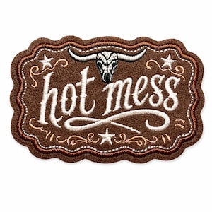 May include: A brown embroidered patch with a scalloped edge featuring the white text hot mess in a cursive script. Above the text is a white embroidered longhorn skull, and the design is accented with white stars and decorative scrollwork.