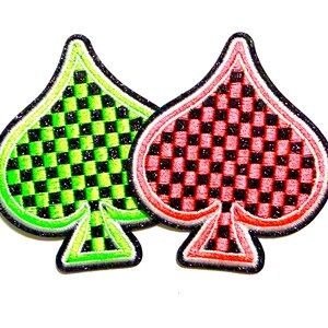 May include: Two embroidered patches in the shape of a spade, a playing card suit. One is green with a black and green checkered pattern, the other is red with a black and red checkered pattern. Both have a glittery border.