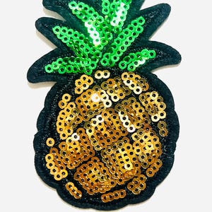 May include: A sequined pineapple patch with a black outline. The pineapple body is covered in gold sequins, while the leaves are green. The patch is approximately 2 inches in height.