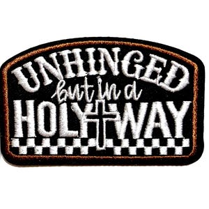 May include: Embroidered patch with the words "UNHINGED but in a HOLY WAY" in white thread on a black background. The patch has a brown border and a cross design. The patch measures approximately 3 inches in length.