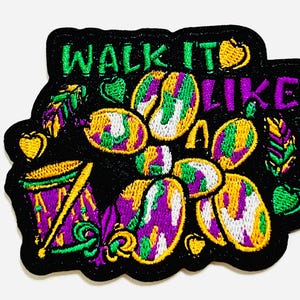 May include: Embroidered patch with the text "WALK IT LIKE" in green and purple. The patch features colorful Mardi Gras beads, a drum, and decorative elements in yellow, green, and purple on a black background.