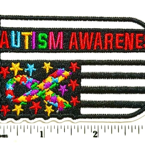 May include: An embroidered patch featuring the text AUTISM AWARENESS in rainbow colors above a black and white flag design with a colorful infinity symbol and stars. A ruler shows the patch is approximately 3.5 inches wide at its base.