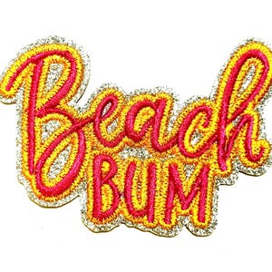 May include: Embroidered patch with the words "Beach Bum" in a cursive font. The text is in bright pink, outlined in yellow, and surrounded by a silver glitter border. The patch is approximately 2.5 inches wide.