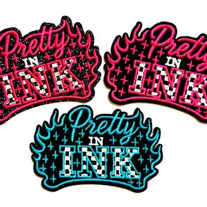 May include: Three embroidered patches with the text "Pretty in Ink". The patches are in a flame design with the text in pink and blue, and the letters "INK" have a checkered pattern.