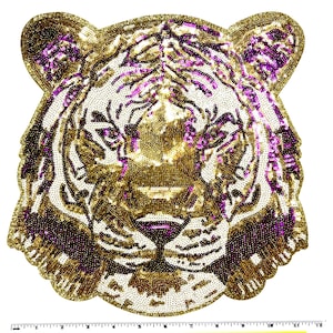 May include: A decorative tiger head patch with gold, purple, and white sequins. The patch features a detailed design of a tiger's face, including eyes, nose, and mouth. The sequins create a shimmering effect, making it suitable for embellishing clothing or accessories.