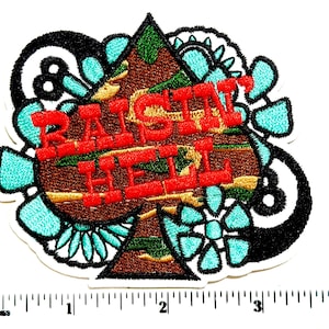 May include: Embroidered patch in the shape of a spade with the words "RAISIN HELL" in red. The spade is brown with green and yellow accents, surrounded by turquoise and black floral designs. The patch is approximately 3 inches wide.