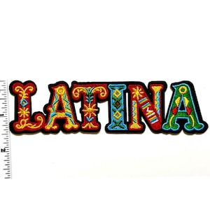 May include: Embroidered patch with the word "LATINA" in colorful, ornate lettering. The letters are outlined in black and feature a variety of designs in red, yellow, blue, and green. A ruler is placed next to the patch for size reference.