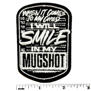 May include: A black and white embroidered patch with a rounded rectangular shape. The text reads: WHEN IT COMES TO MY CHILD I WILL SMILE IN MY MUGSHOT. A white ruler is visible at the bottom, showing the patch is approximately 3 inches tall.