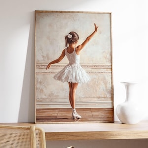 May include: A framed painting of a young ballerina wearing a white tutu and pointe shoes. The ballerina is standing on a wooden floor with a white wall behind her. The painting is in a light brown frame.