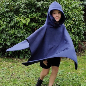 May include: A child wearing a navy blue hooded poncho with a pocket. The poncho is made of fleece and has a drawstring hood. The child is standing in a grassy area.
