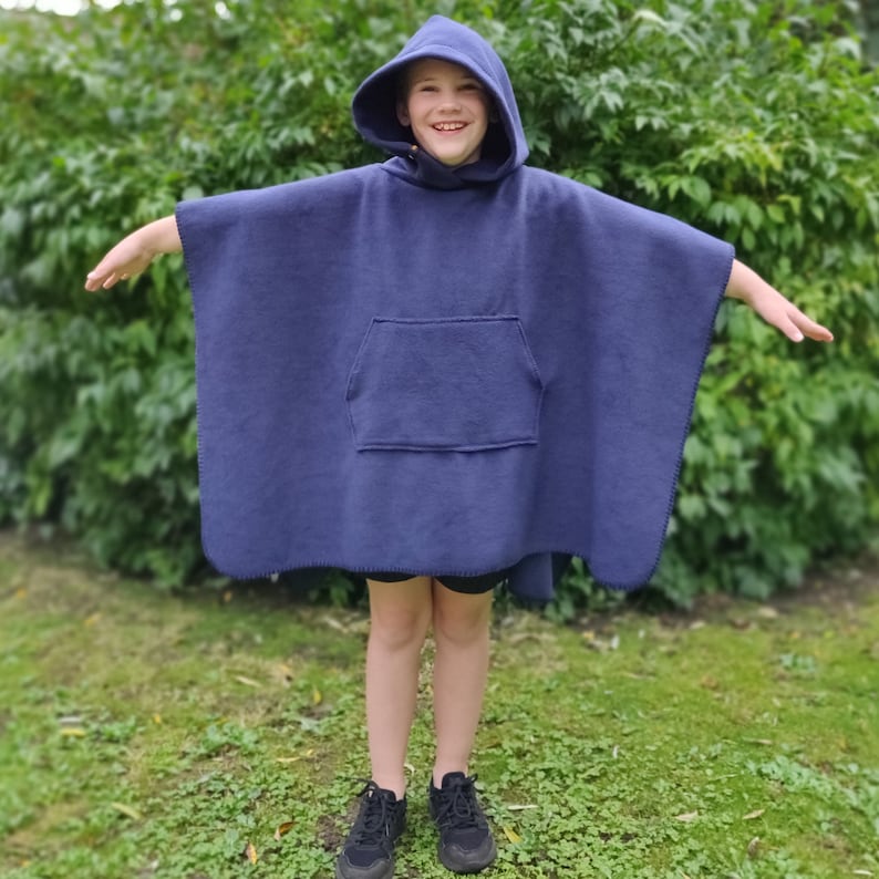 May include: A navy blue hooded fleece poncho with a front pocket. The poncho is worn by a person standing in a grassy area.