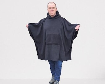 May include: A black fleece hooded poncho with a large pocket on the front. The poncho is being worn by a person standing in front of a white background.