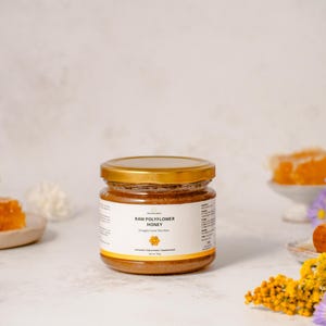 May include: A glass jar of raw polyflower honey with a gold lid. The label reads "Raw Polyflower Honey" and "Straight From The Hive".