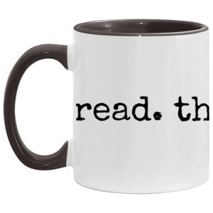 May include: White ceramic coffee mug with a black interior and handle. The mug has the text "read. the" printed in black on the front.