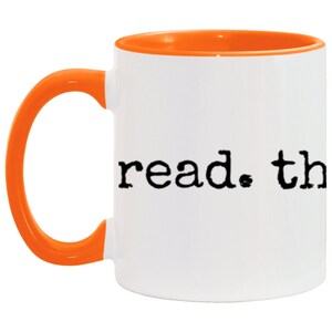 May include: White ceramic mug with an orange rim and handle. The mug has the text "read. the" printed on the front in a typewriter font.