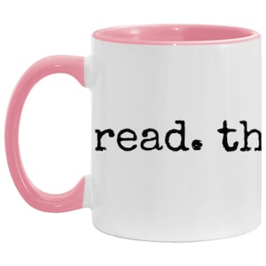 May include: White ceramic mug with a pink rim and handle. The mug has the text "read. the" printed in black.