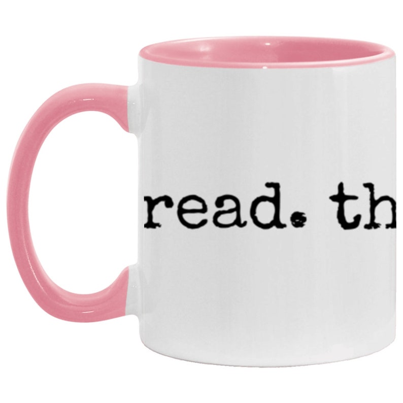 May include: White ceramic mug with a pink rim and handle. The mug has the text "read. the" printed in black.