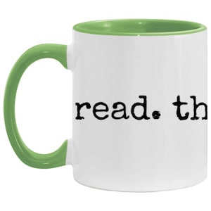 May include: White ceramic coffee mug with a green rim and handle. The mug has the text "read. the" printed on the front in a typewriter font.