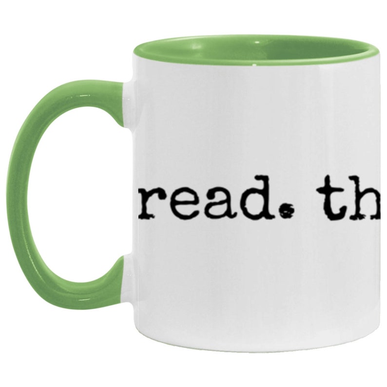 May include: White ceramic coffee mug with a green rim and handle. The mug has the text "read. the" printed on the front in a typewriter font.