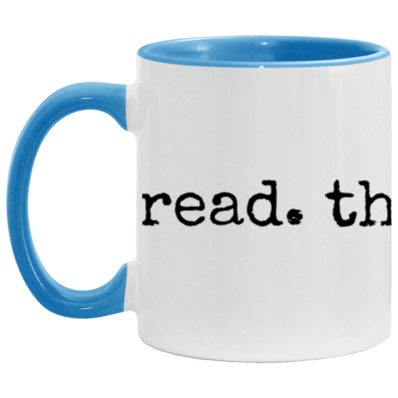 May include: White ceramic coffee mug with a light blue rim and handle. The mug has the text "read. the" printed in black.