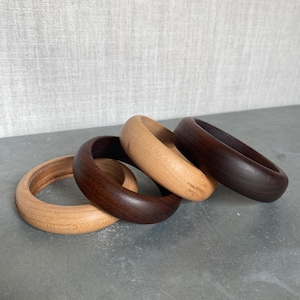 May include: Four wooden bangles, two light brown and two dark brown, stacked on a gray surface.