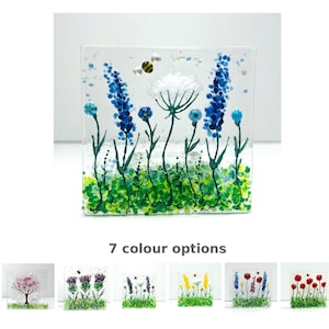 May include: A clear glass square with a floral design. The artwork features blue flowers, green grass, and a bee. The text "7 colour options" is below the main image, with examples of other colour variations.