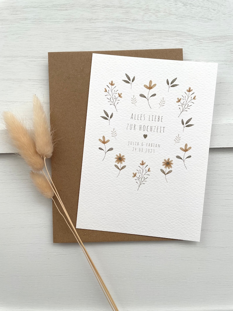 May include: A white card with a floral design and the text "Alles Liebe zur Hochzeit" with a heart symbol and the date "24.04.2023" and the names "Julia & Fabian".