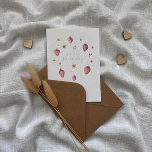 May include: A white card with a watercolor illustration of strawberries and flowers. The text "Happy Birthday" is written in a cursive font.