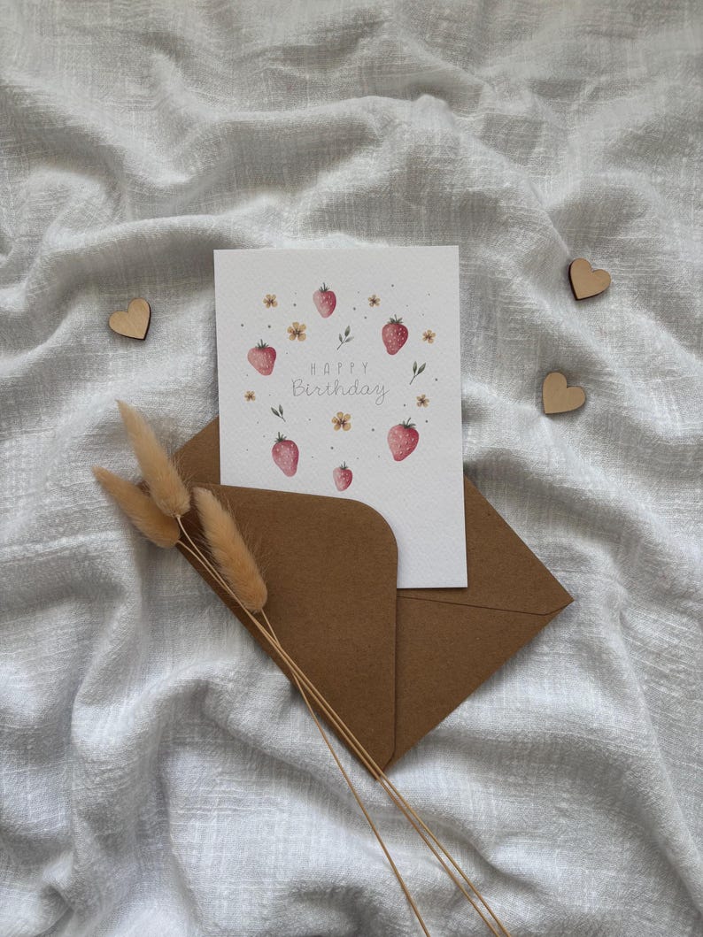 May include: A white card with a watercolor illustration of strawberries and flowers. The text "Happy Birthday" is written in a cursive font.