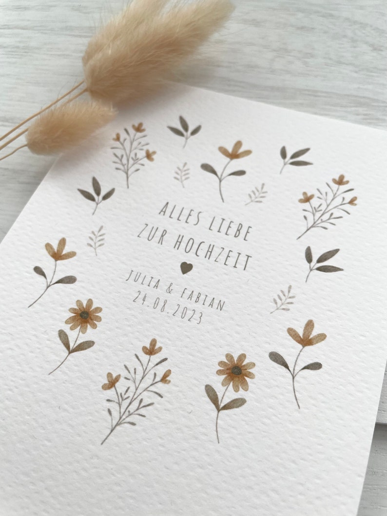 May include: A white card with brown floral illustrations and the text "Alles Liebe zur Hochzeit" with a heart symbol. Below the text is "Julia & Fabian 24.08.2023".