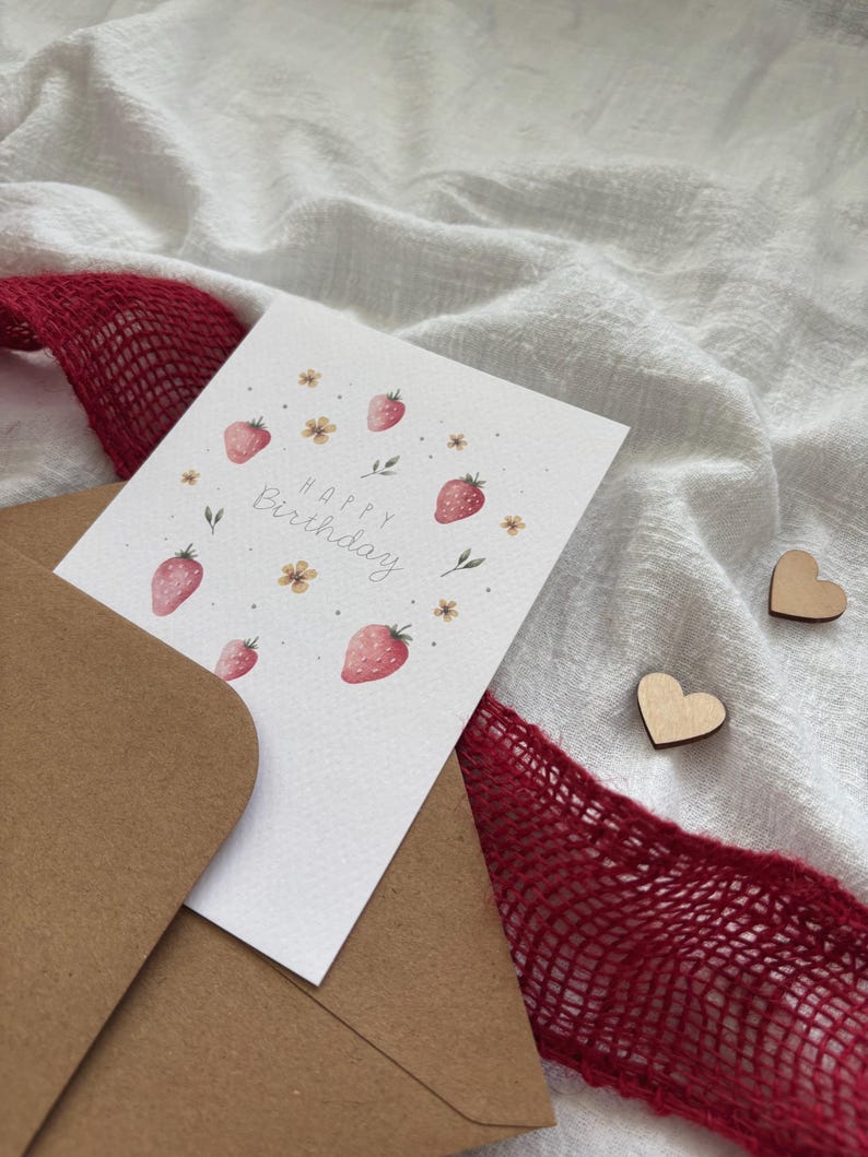 May include: A white card with a brown envelope. The card has a watercolor illustration of strawberries and flowers. The text "Happy Birthday" is written in cursive on the card.
