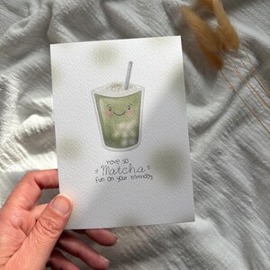 Puede incluir: Tarjeta de cumplea&ntilde;os de acuarela con un dibujo de matcha sonriente con pajita. La tarjeta tiene el texto "have so Matcha fun on your birthday" en fuente manuscrita. La tarjeta es blanca con detalles verdes.