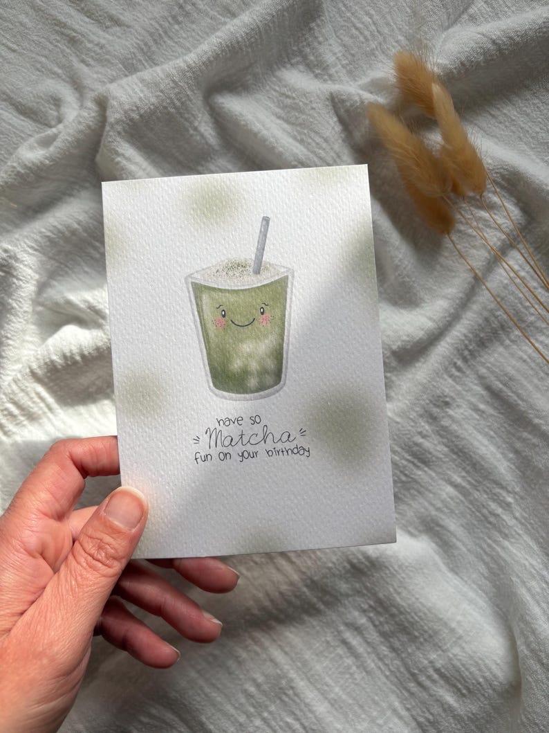 Puede incluir: Tarjeta de cumplea&ntilde;os de acuarela con un dibujo de matcha sonriente con pajita. La tarjeta tiene el texto "have so Matcha fun on your birthday" en fuente manuscrita. La tarjeta es blanca con detalles verdes.