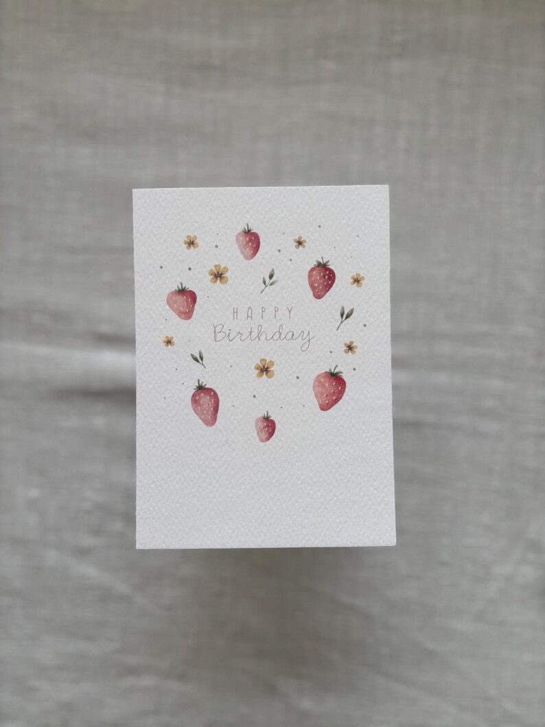 May include: A white card with a watercolor illustration of strawberries and flowers. The text "Happy Birthday" is written in cursive.