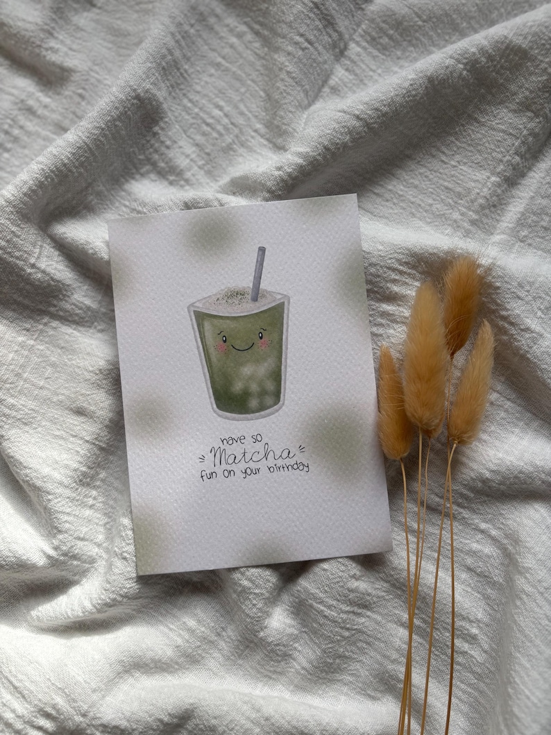 Puede incluir: Tarjeta de felicitaci&oacute;n de cumplea&ntilde;os con una ilustraci&oacute;n de bebida de matcha. La tarjeta presenta una bebida de matcha sonriente con una pajita y el texto "have so Matcha fun on your birthday". La tarjeta est&aacute; sobre un fondo blanco con un efecto acuarela verde claro.
