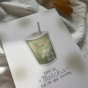 Puede incluir: Tarjeta de felicitaci&oacute;n de acuarela con un dibujo de bebida matcha sonriente y una pajita. El texto "have so Matcha fun on your birthday" est&aacute; escrito en negro. Fondo blanco texturizado.