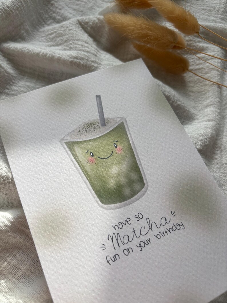 Puede incluir: Tarjeta de felicitaci&oacute;n de acuarela con un dibujo de bebida matcha sonriente y una pajita. El texto "have so Matcha fun on your birthday" est&aacute; escrito en negro. Fondo blanco texturizado.