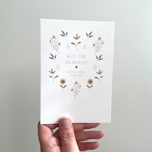 May include: A white card with a floral design and the text "Alles Liebe zur Hochzeit" with the names "Julia & Fabian" and the date "24.06.2023".
