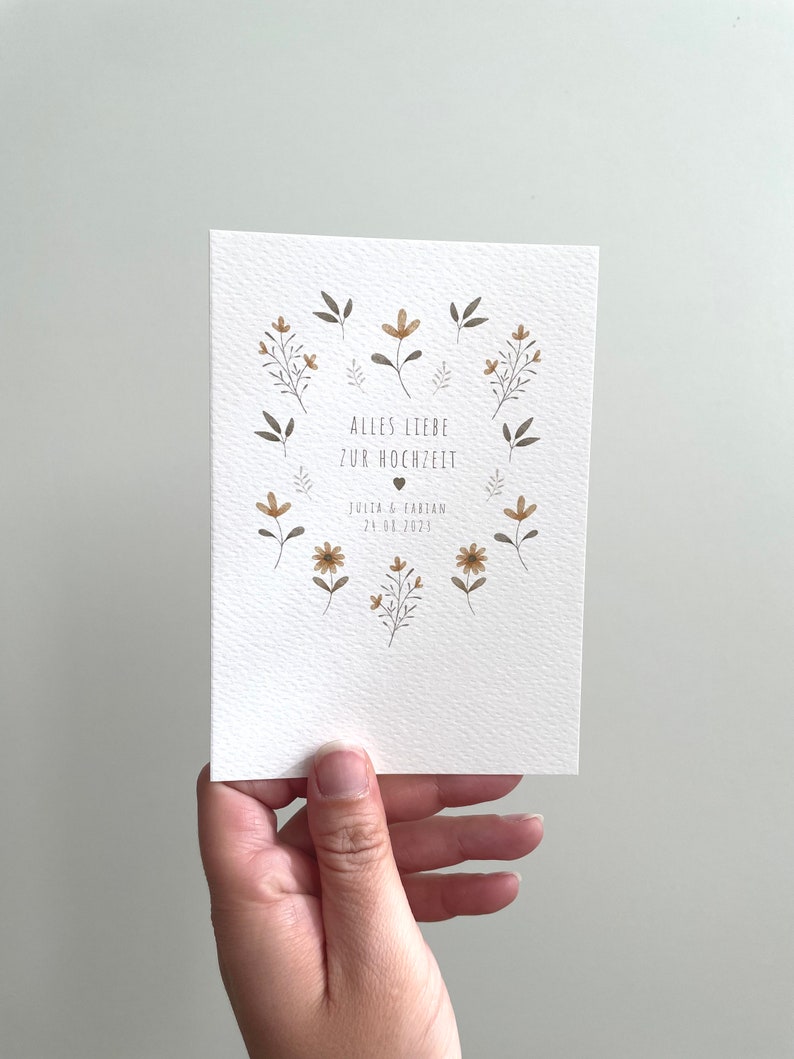 May include: A white card with a floral design and the text "Alles Liebe zur Hochzeit" with the names "Julia & Fabian" and the date "24.06.2023".