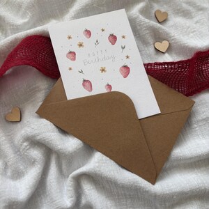 May include: A brown envelope with a white card inside. The card has a watercolor illustration of strawberries and flowers with the text "Happy Birthday".