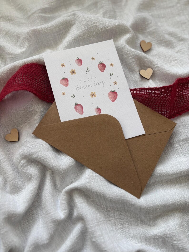May include: A brown envelope with a white card inside. The card has a watercolor illustration of strawberries and flowers with the text "Happy Birthday".