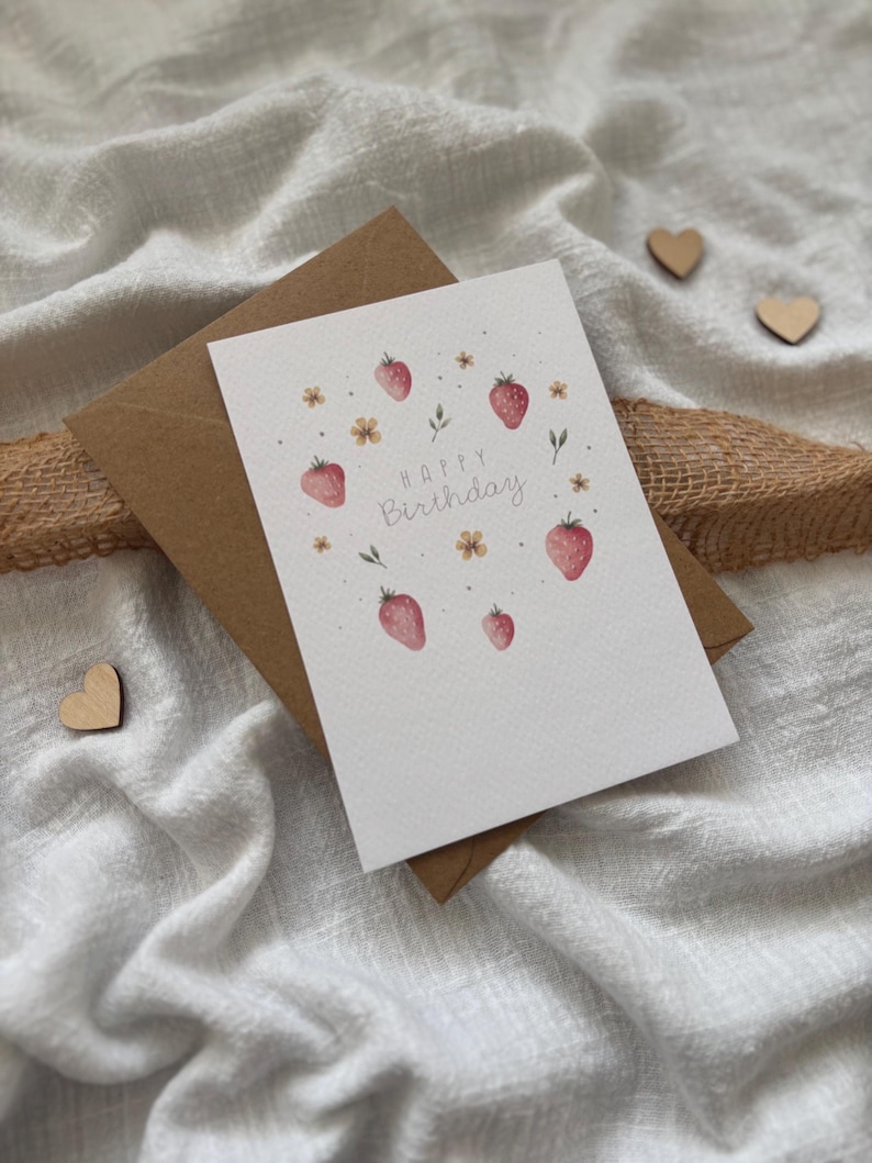 May include: A white card with a pink and green watercolor illustration of strawberries and flowers. The card says "Happy Birthday" in a pink script font.