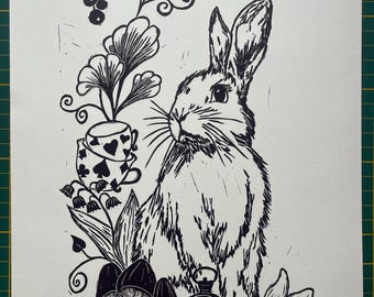 May include: Black and white linocut print featuring a rabbit, mushrooms, and a pocket watch. A teacup with a spade design and the text "No time!" are also included. The print has a whimsical, illustrative style.