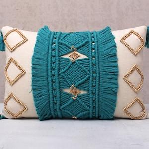 May include: A decorative throw pillow with a teal and white geometric pattern. The pillow has a fringe border and wooden bead accents.