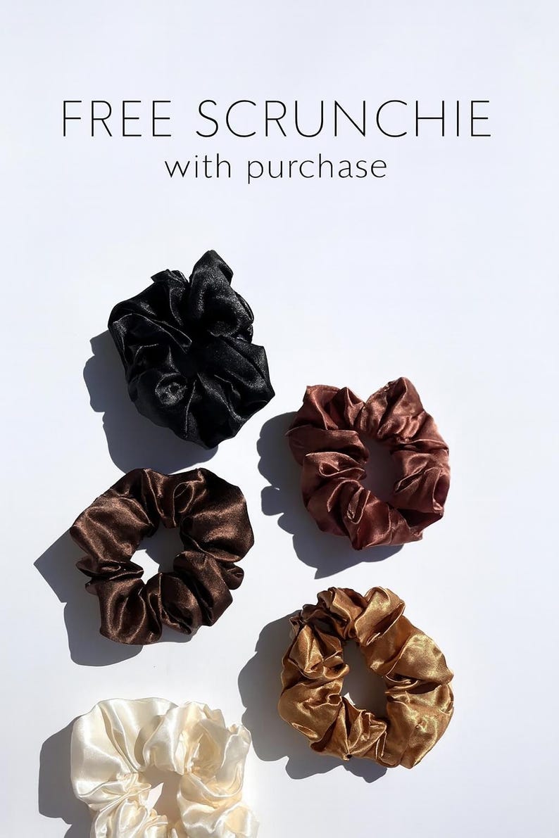 K&ouml;nnte beinhalten: Eine Auswahl an Satin-Haargummis in verschiedenen Farben, darunter Schwarz, Braun und Gold, wird auf wei&szlig;em Hintergrund pr&auml;sentiert. Der Text "FREE SCRUNCHIE with purchase" ist ebenfalls zu sehen. Diese Haaraccessoires sind ideal, um jedem Haarschnitt einen Hauch von Eleganz zu verleihen.