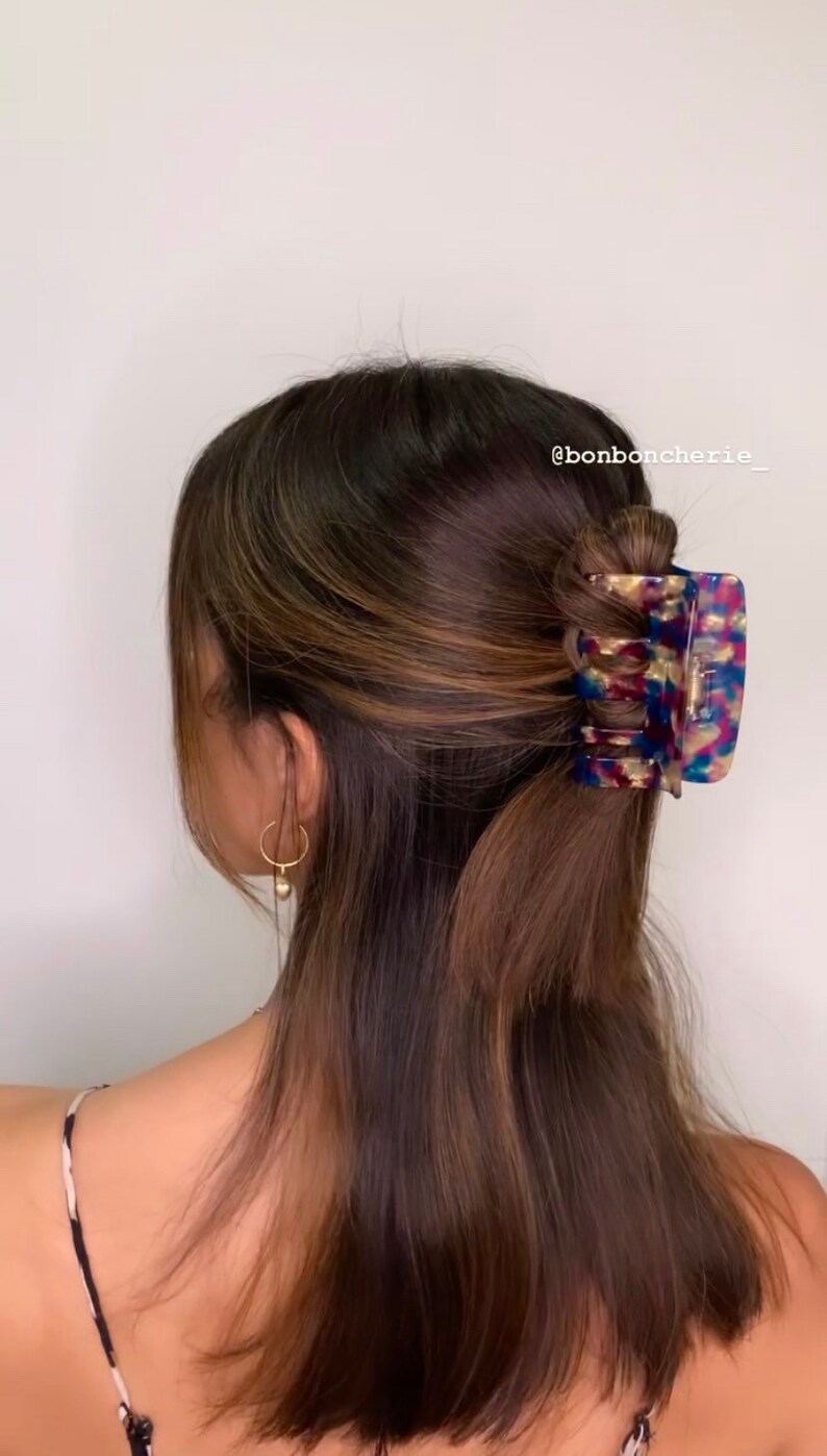 K&ouml;nnte beinhalten: Eine Haarspange mit Schildpattmuster, in Blau-, Gold- und Lilat&ouml;nen, h&auml;lt einen Teil braunen Haares. Der Text "bonboncherie_" ist rechts oben sichtbar. Die Haare sind halb hochgesteckt, halb offen.