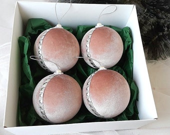Puede incluir: Cuatro adornos navideños de terciopelo rosa empolvado con ribetes plateados y un acento de perla. Los adornos están en una caja blanca con papel de seda verde.